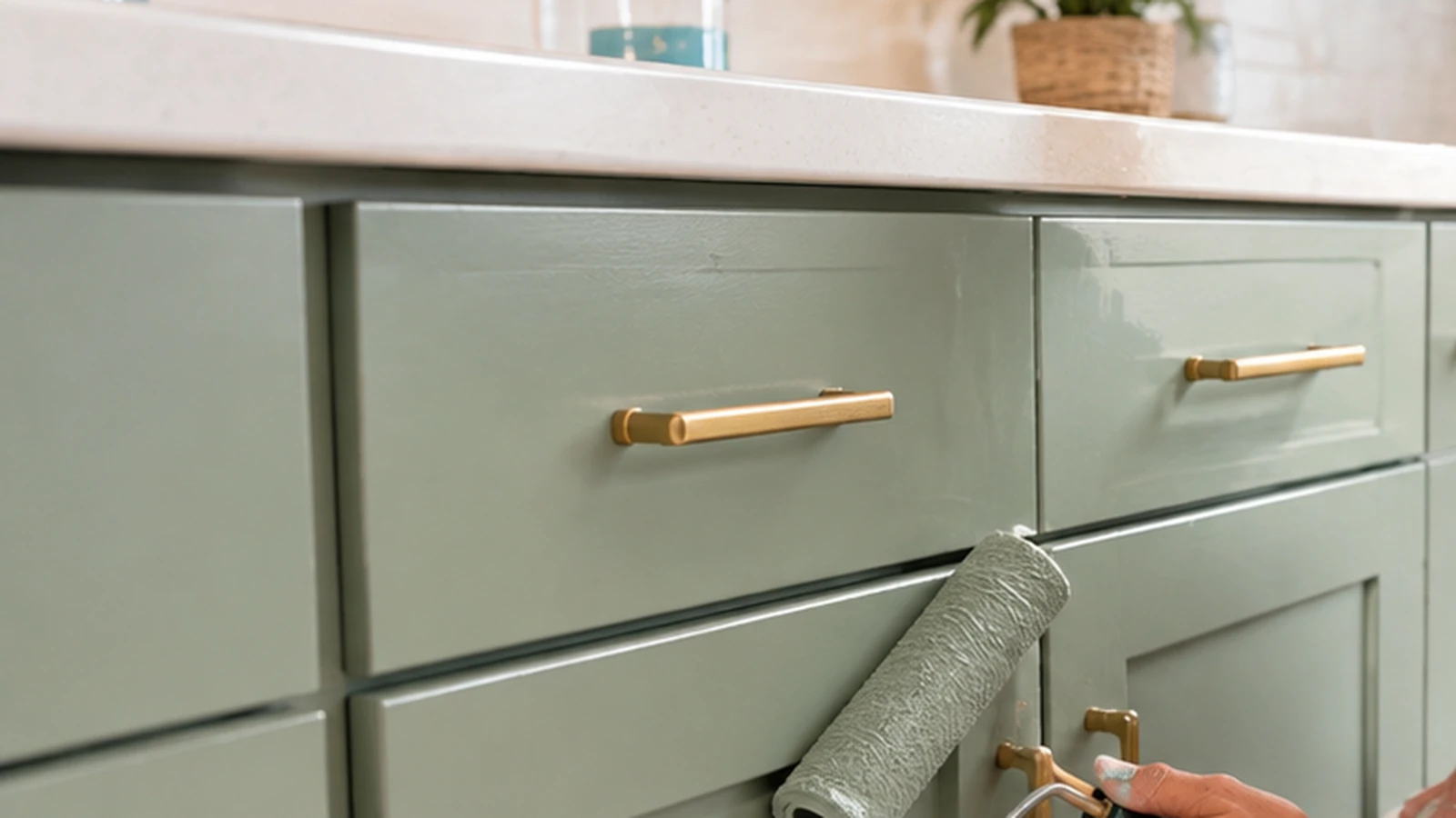 Freshly painted sage-green residential kitchen cabinets with a paint roller